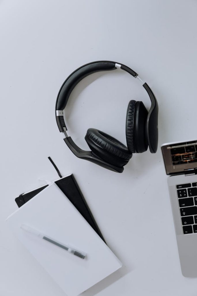 Flat lay of headphones, laptop, and notebook in a modern home office setup.